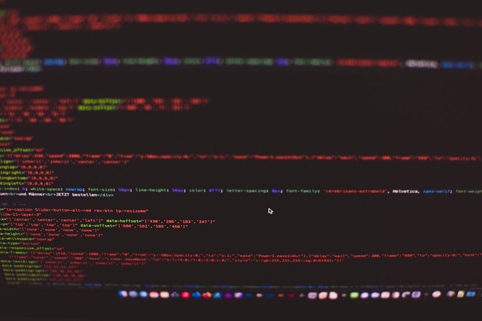 A close-up photograph of a computer screen displaying a code editor with multicolored lines of HTML and CSS code on a black background. The code includes tags, attributes, and styling elements in red,