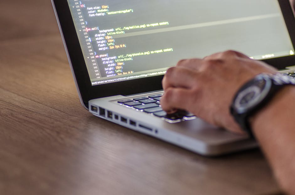 A close-up photograph of a computer screen displaying a code editor with multicolored lines of HTML and CSS code on a black background. The code includes tags, attributes, and styling elements in red,